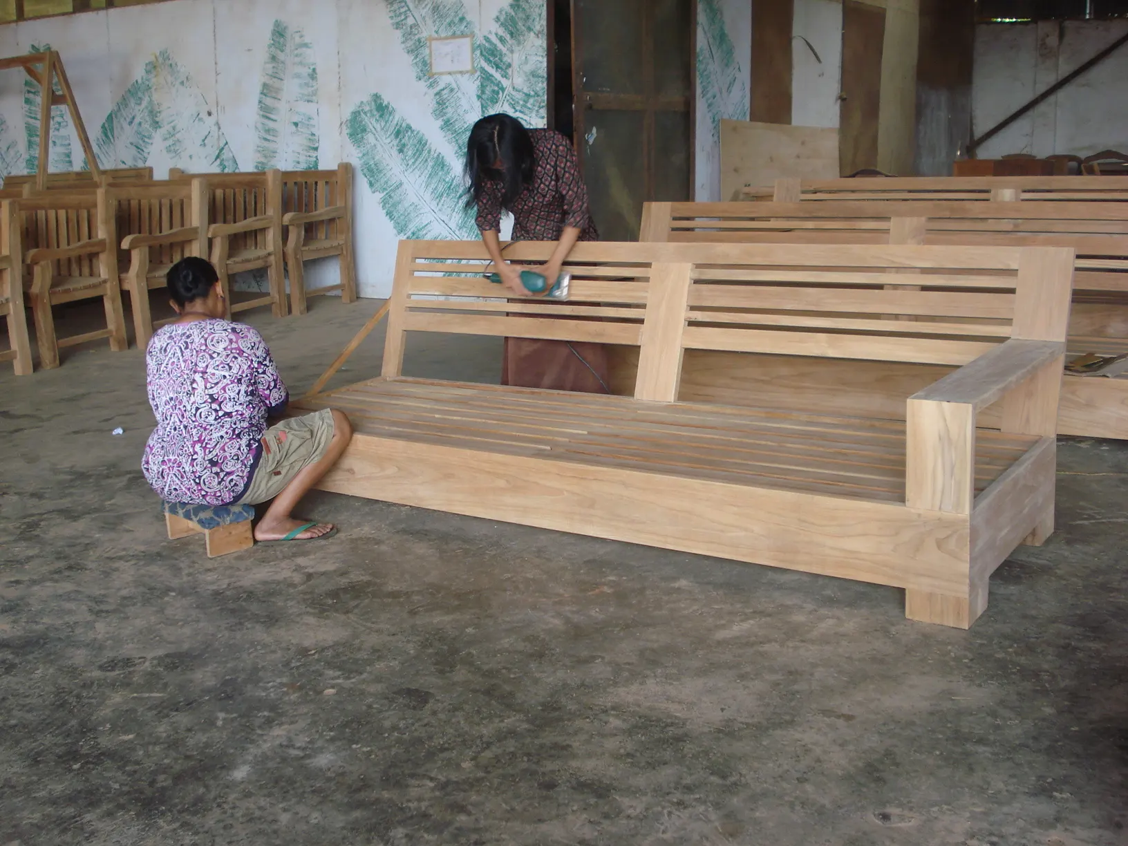 Artisans ponçant un canapé en teck massif dans un atelier partenaire à Bali