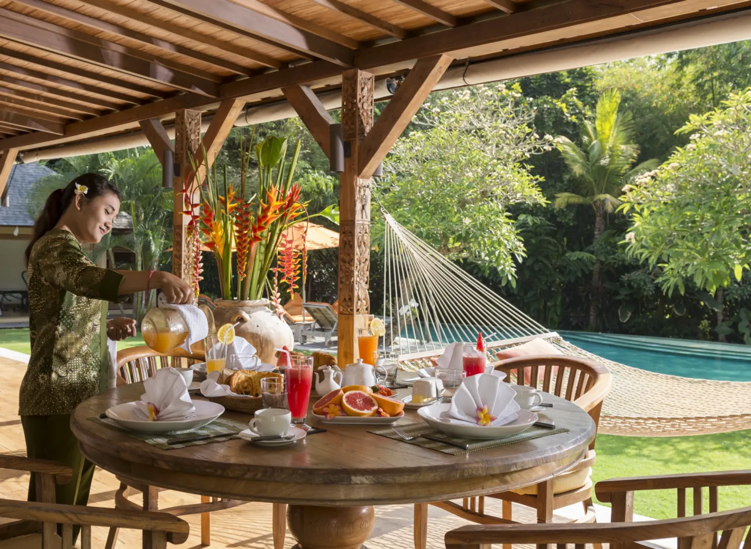 Table ronde en teck sous une pergola, petit-déjeuner servi